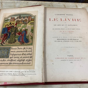 Op de afbeelding: Een open boek met een rode leren kaft. De linkerpagina toont een handgeschilderde illustratie van een man die een boek aan een andere man in een tuin overhandigt. De rechterpagina toont de titel "L'ANCIENNE FRANCE. LE LIVRE LES ARTS QUI S'Y BATTACHENT LES ORIGINES JUSQU'A LA FIN DU XVIE SIECLE. Par M. P. LOUISY."