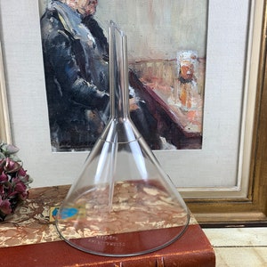 May include: A clear glass funnel with a long, narrow spout. The funnel is sitting on a brown, marbled surface.