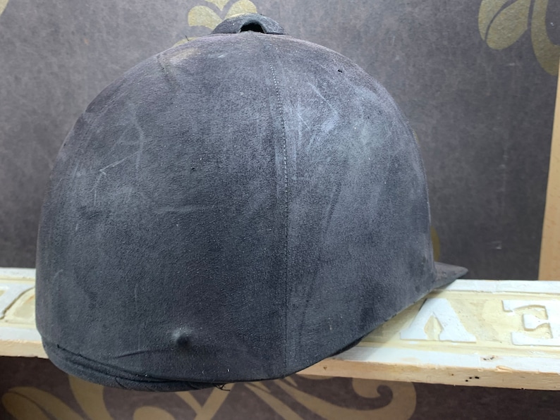 May include: A black riding helmet with a smooth, slightly textured surface. The helmet has a seam down the center of the back.