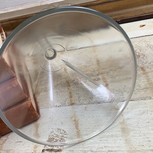 May include: A clear glass funnel with a wide mouth and a narrow spout. The funnel is resting on a wooden surface.