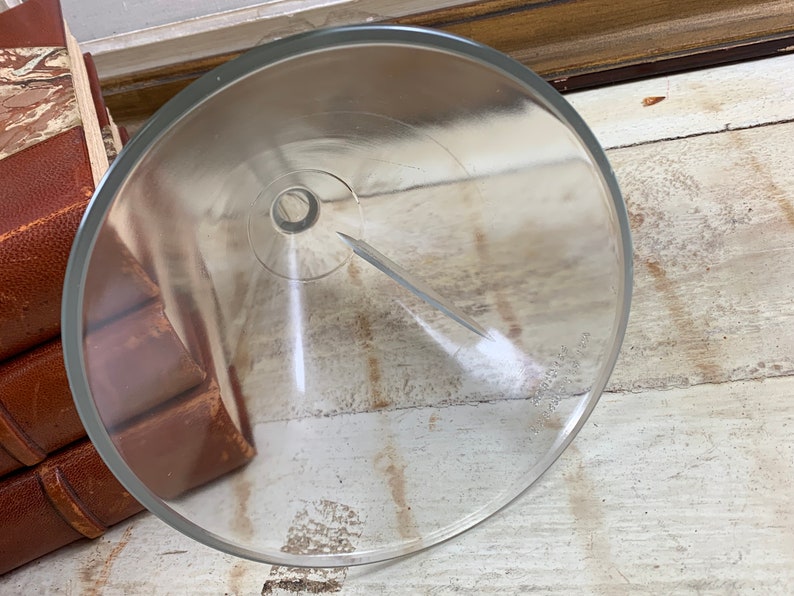 May include: A clear glass funnel with a wide mouth and a narrow spout. The funnel is resting on a wooden surface.