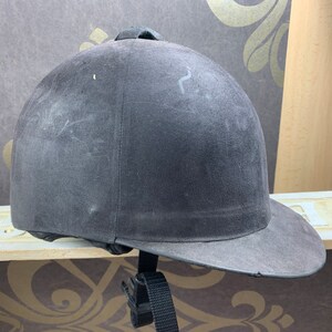 May include: A black riding helmet with a black brim and a black strap. The helmet is made of a soft, suede-like material.