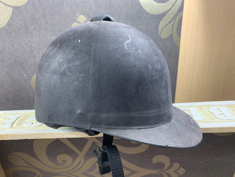 May include: A black riding helmet with a black brim and a black strap. The helmet is made of a soft, suede-like material.