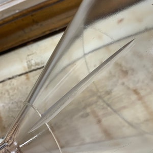 May include: A clear glass funnel with a long, thin, metal rod inside. The funnel is resting on a white surface.