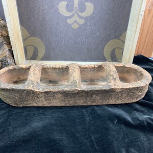 Op de afbeelding: Een rustieke terracotta plantenbak met drie aparte compartimenten. De plantenbak is ovaalvormig en heeft een ruw, getextureerd oppervlak.