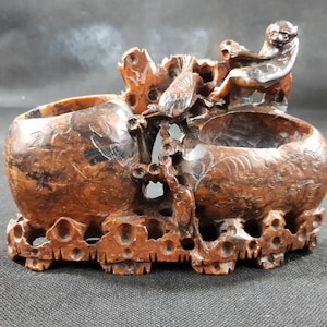Puede incluir: Escultura de madera tallada con dos compartimentos en forma de cuenco conectados por ramas talladas y una figura de mono. La escultura marrón presenta detalles intrincados, incluido un pájaro posado en una rama. La base tiene un diseño calado.