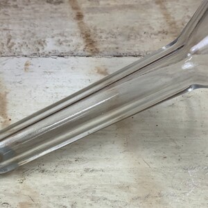 May include: A clear plastic funnel with a long, narrow spout. The funnel has a ribbed design and is made of a durable material.