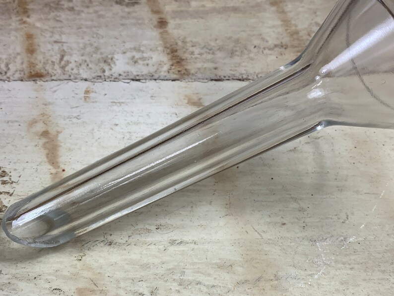 May include: A clear plastic funnel with a long, narrow spout. The funnel has a ribbed design and is made of a durable material.