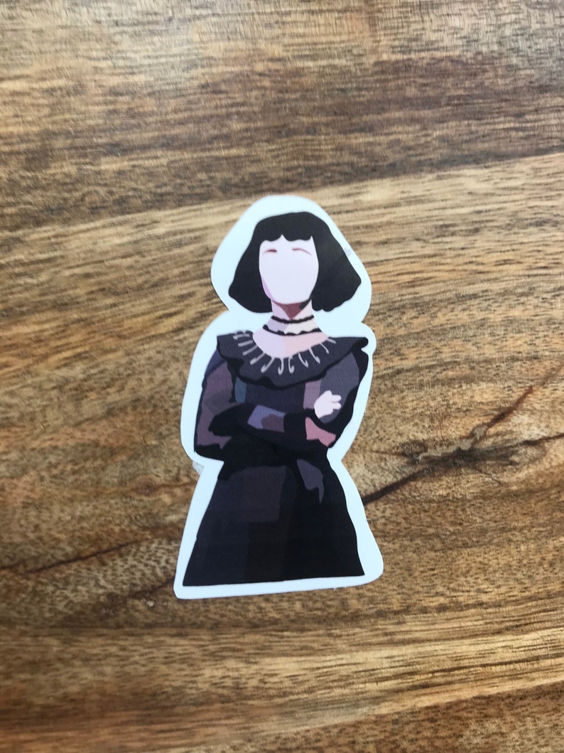 May include: A sticker featuring a stylized illustration of a woman in a dark dress with a high collar and short black hair. The woman has her arms crossed and is set against a white background. The sticker is likely for decorative purposes.