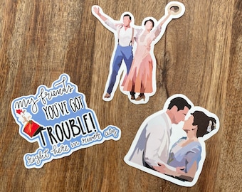 Peut inclure: Trois autocollants représentant des personnages de la comédie musicale "The Music Man". Un autocollant montre un couple dansant, un autre montre un couple en train de s'embrasser, et le troisième autocollant présente le texte "Mes amis, vous avez des ennuis ! Juste ici à River City."