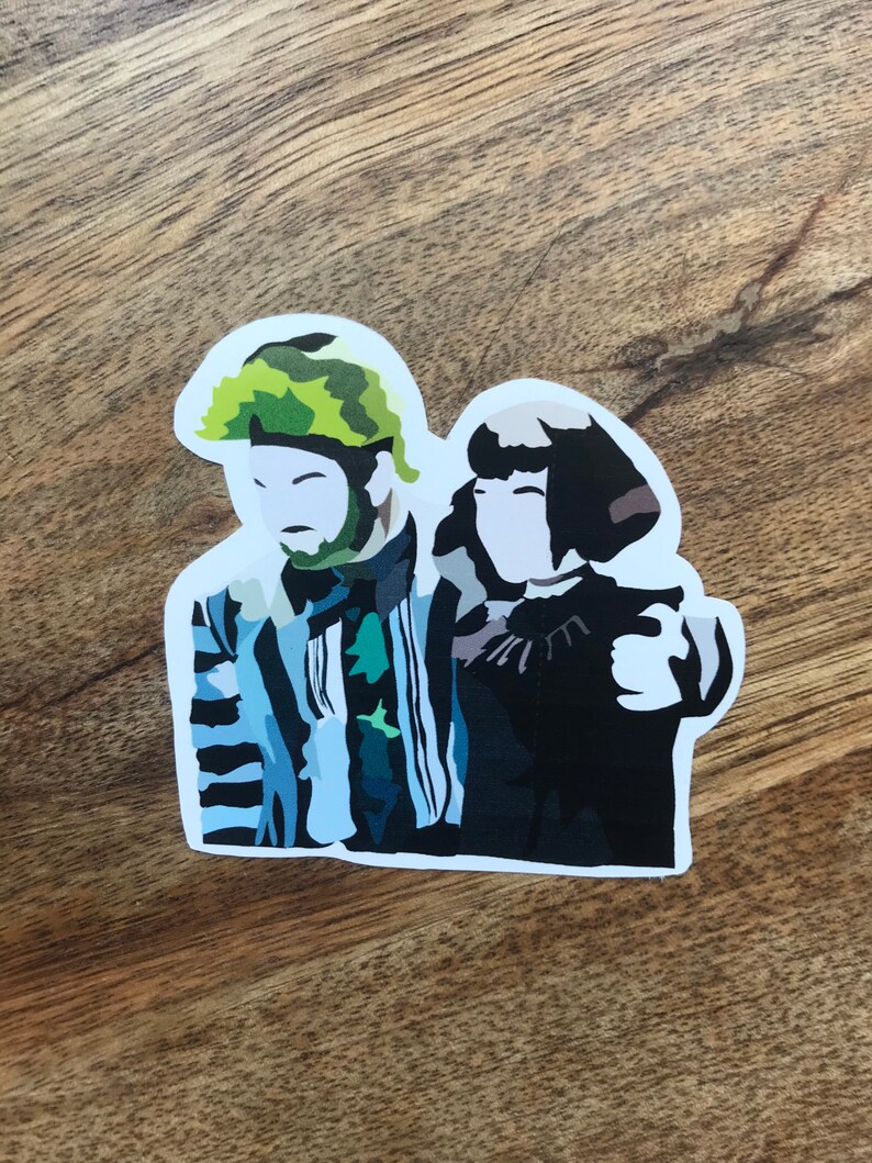 May include: A sticker featuring a stylized illustration of two characters. One character has a green and brown camouflage-patterned hair and beard, and the other has short black hair. The first character is wearing a striped suit with blue and black stripes.