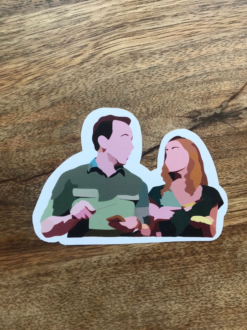 May include: A die-cut sticker featuring a stylized illustration of two people. The man is wearing a green shirt, and the woman is wearing a dark green top. The sticker has a white border and is set against a wooden background.