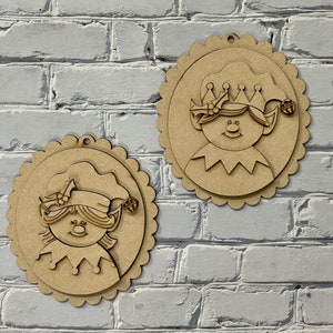 May include: Two unfinished wooden elf ornaments with scalloped edges. Each ornament features a smiling elf face with a hat and collar. One elf wears a crown. The ornaments are designed for hanging.