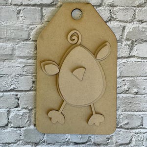 May include: A wooden tag with a cutout design of a cartoon chick. The chick has an egg-shaped body, small wings, and feet. The tag is light brown and has a hole at the top for hanging.