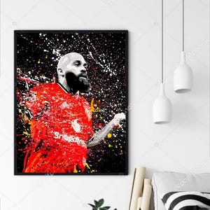 May include: Framed art print featuring a stylized portrait of a bald man with a beard in a red jersey. The artwork has a splatter paint effect with red, white, yellow, and black colors. The background is black.