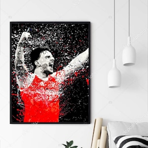 May include: A framed art print featuring a stylized image of a soccer player celebrating. The player is depicted in a red and white jersey against a black background with red and white paint splatter effects. The artwork is in a black frame.