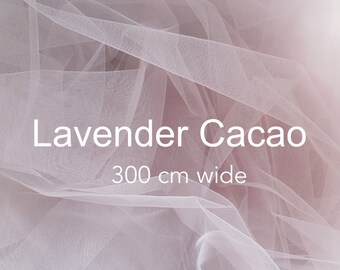May include: A close-up of a sheer, light lavender fabric with a delicate texture. The fabric is draped and folded, showcasing its soft and airy quality. The text "Lavender Cacao 300 cm wide" is printed on the fabric.