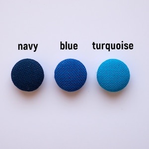 Op de afbeelding: Drie met stof beklede knoppen in marineblauw, blauw en turquoise.