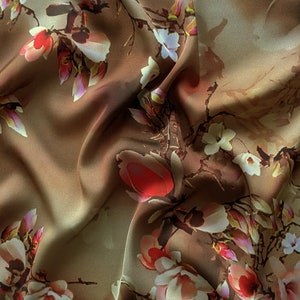 May include: A brown fabric with a floral print featuring white, pink, and red flowers. The fabric has a soft, silky texture.