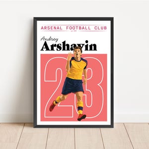 Pode incluir: Pôster emoldurado com Andrey Arshavin com o uniforme do Arsenal Football Club. O pôster tem um fundo vermelho com o número 23 em branco. O jogador é retratado em ação, vestindo uma camisa amarela e azul marinho.