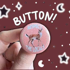 May include: A pink button with a white border and a deer illustration. The button says "Respect the Locals".
