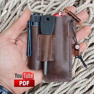 May include: A brown leather pocket organizer with a small pocket for a lighter or a small tool. The organizer has a snap closure and a loop for a lanyard. The organizer is being held in a hand.