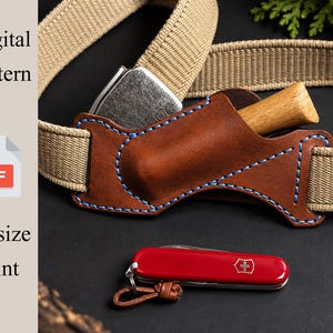 Op de afbeelding: Een bruin lederen schede met blauwe stiksels bevestigd aan een beige geweven riem, met daarin een klein mes met houten handvat. Een rood multifunctioneel gereedschap met een leren koordje ligt eronder. Tekst: Digital Pattern, PDF, A4 size Print.