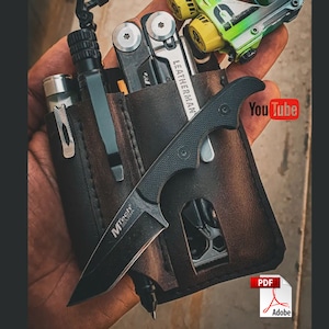 Może przedstawiać: Brązowy skórzany organizer do kieszeni z czarnym nożem, wielofunkcyjnym narzędziem i latarką. Nóż ma czarną rękojeść i srebrne ostrze. Wielofunkcyjne narzędzie ma srebrną rękojeść i różne narzędzia. Latarka ma czarną rękojeść i srebrną głowicę. Organizer ma nadrukowany napis "LEATHERMAN".