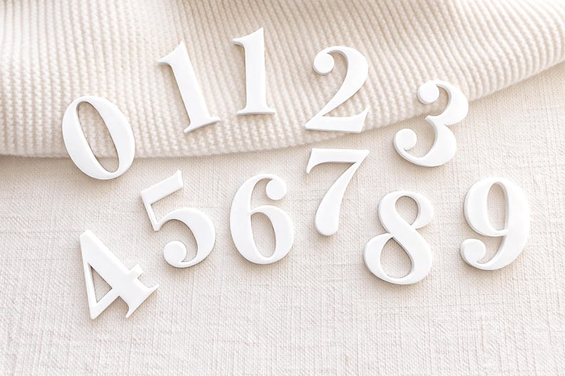 White acrylic number set for monthly baby milestone sign (0–9 plus extra 1), shown on neutral textured fabric background.