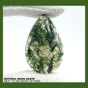 May include: A teardrop-shaped moss agate cabochon with a green and white pattern. The stone is translucent and has a natural, organic look.