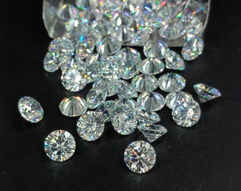 May include: A large group of clear, round, faceted gemstones, likely diamonds, scattered on a black surface. The gemstones are reflecting light, creating a rainbow effect.