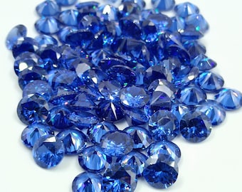 May include: A large pile of loose, faceted, sapphire blue gemstones. The gemstones are round and have a brilliant, sparkly finish.
