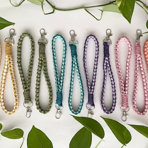 May include: Ten colorful braided keychains with silver key rings. The keychains are made of a soft, woven material and come in a variety of colors, including yellow, green, blue, purple, pink, and orange.