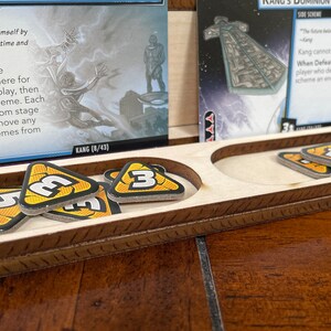 May include: A wooden game board with two slots for holding game pieces. The slots are filled with yellow and black triangular tokens with the number "3" printed on them. The board has a brown wooden frame with a decorative pattern.