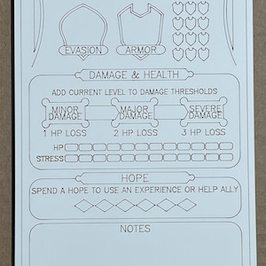 May include: A white game card with black line art. The card features sections for Evasion, Armor, Damage & Health, and Hope. Text includes "Minor Damage," "Major Damage," and "Severe Damage." There are also spaces for HP and Stress.