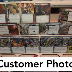 May include: A collection of trading cards featuring characters and scenes from the Marvel Cinematic Universe. The cards are displayed in a wooden rack with a label that reads "Customer Photo".