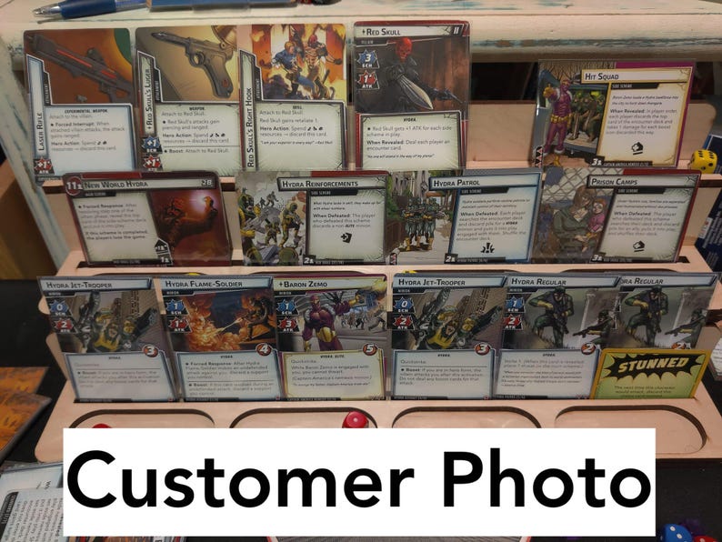 May include: A collection of trading cards featuring characters and scenes from the Marvel Cinematic Universe. The cards are displayed in a wooden rack with a label that reads "Customer Photo".