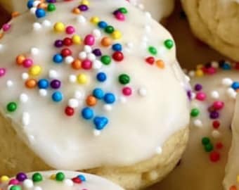 Puede incluir: Primer plano de varias galletas italianas, cada una con un glaseado de color claro y chispas coloridas. Las galletas son redondas y ligeramente abovedadas, con una apariencia suave y atractiva. Las chispas añaden un toque festivo.