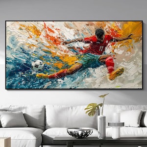 May include: Abstract painting of a soccer player in action, kicking the ball. The artwork features a dynamic composition with vibrant colors, including red, blue, yellow, and white. The player is wearing a red jersey and green shorts. The painting is framed in black.