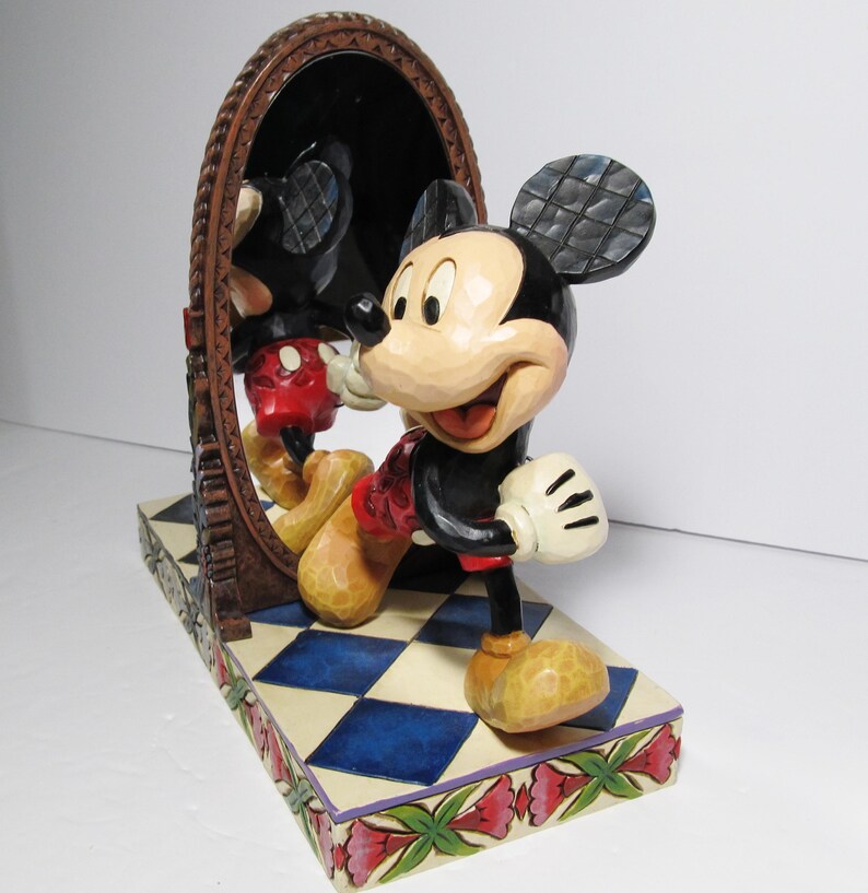 以下が含まれることがあります： 茶色のフレームの楕円形の鏡の前に立つミッキーマウスの樹脂製フィギュア。キャラクターは黒い耳、クリーム色の顔、赤いショートパンツ、黄色い靴を身に着けています。台座は青と白の市松模様で、花柄の縁取りが施されています。