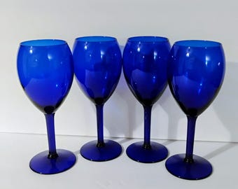 May include: A set of four matching wine glasses crafted from deep cobalt blue glass. Each glass features a rounded bowl, a slender stem, and a circular base, all rendered in a consistent, solid, and vibrant blue color throughout the entire structure.