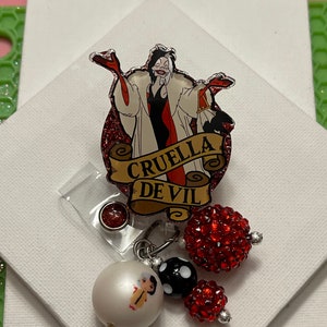 May include: A red and black glitter badge holder with a cartoon image of Cruella De Vil and the text "Cruella De Vil". The badge holder has a red and black beaded charm attached.