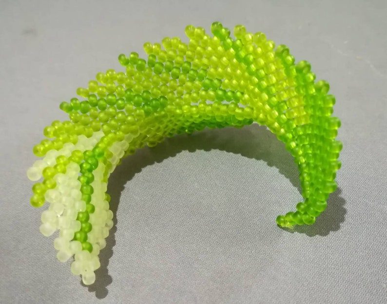May include: A green and white beaded sculpture in the shape of a wave. The beads are arranged in a spiral pattern, creating a dynamic and textured effect.