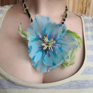 May include: A blue beaded flower necklace with green leaves and a black cord. The flower is made of blue, purple, and white beads.