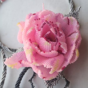 May include: A pink beaded rose with a silver and black beaded stem. The rose is a part of a beaded necklace.