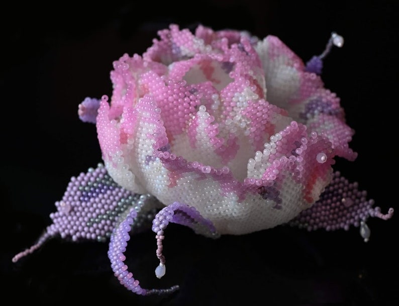 May include: A delicate pink and purple beaded flower with a white center. The flower is made of small beads and has a realistic appearance.