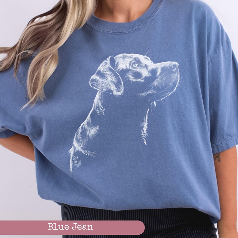 May include: A blue jean t-shirt with a white outline of a Labrador Retriever dog looking to the right.