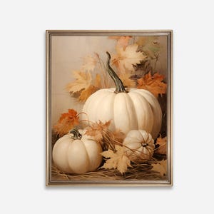 May include: A framed still life painting featuring three white pumpkins of varying sizes, surrounded by autumn leaves in shades of orange and yellow. The pumpkins are set against a neutral background, creating a warm, seasonal aesthetic.