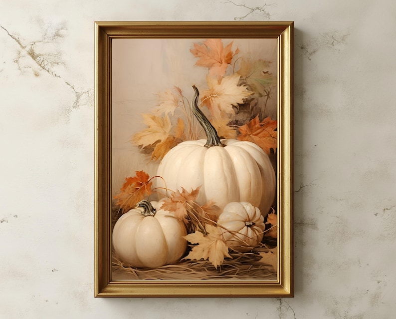 May include: A framed autumn still life featuring three white pumpkins of varying sizes, surrounded by orange and yellow fall leaves. The artwork is set against a soft, neutral background, and framed in a gold-colored frame.