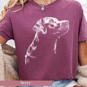 May include: A maroon t-shirt with a white outline drawing of a black labrador retriever's head. The dog is looking to the right and has its mouth closed. The text "Berry" is printed below the image.